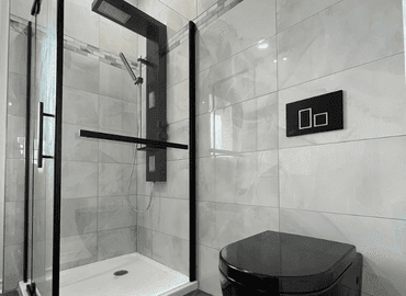 Douche vitrée avec colonne de douche noire et toilette suspendue