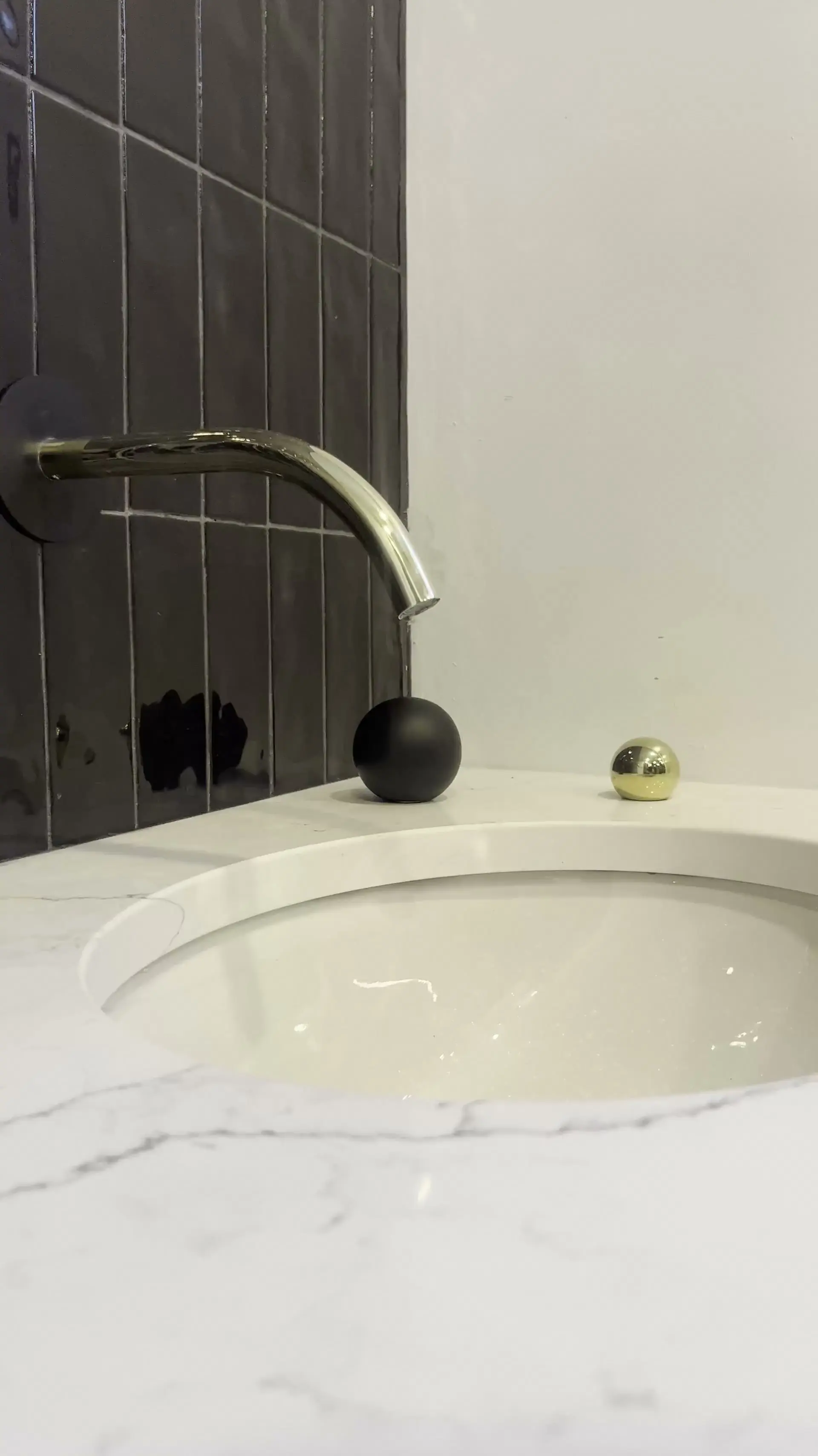Robinet mural doré au-dessus d’un lavabo encastré dans un comptoir effet marbre, devant une céramique noire